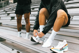 Runner lacing up in white crew socks on stadium bleachers